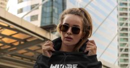 Stylish model in a black hoodie with "WE ARE HARDTEKK" design, showcasing urban fashion in a cityscape.