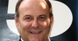 Gerry Scotti smiles while wearing a black suit and white shirt, embodying his charismatic presence in Italian entertainment.