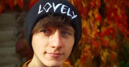 Young man in a beanie poses against vibrant autumn leaves, showcasing a casual style and a charming expression.