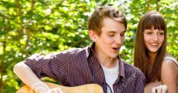 Young couple enjoying a moment outdoors, with a guitar, singing together amidst nature's greenery.