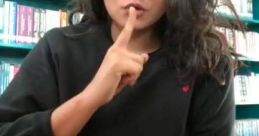 Person making a shushing gesture in a library setting, emphasizing quietness while using a laptop. Boob Tube Library.
