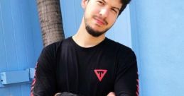 Young man in a black Typical Gamer t-shirt posing confidently among cacti against a blue background.