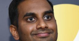 Aziz Ansari smiling confidently in a stylish black outfit at a red carpet event, showcasing his charm and presence.
