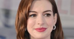 Anne Hathaway smiles warmly at a public event, showcasing her stylish floral blouse and glossy, wavy hair.