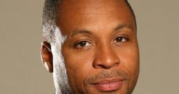 Professional headshot of Gus Johnson, showcasing his polished look with a black suit and purple tie against a neutral background.