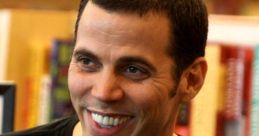 Steve-O smiles in a casual black shirt, showcasing his charismatic personality in a cozy bookshop setting.