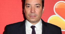Jimmy Fallon poses in a sharp black suit against a vibrant red background, showcasing his signature style and charisma.