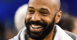 Thierry Henry smiling while wearing a grey Adidas hoodie, showcasing his charismatic personality and passion for soccer.