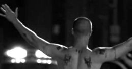 A man with tattoos raises his arms in a dramatic posture, captured in a tense urban setting reminiscent of "American History X.
