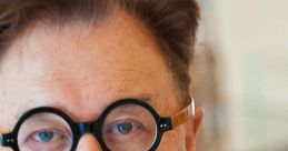 Mr. Chow poses confidently, showcasing his unique round glasses and distinguished style in a sophisticated setting.
