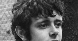 Young man with curly hair, wearing a striped jacket, posed thoughtfully against a tree, capturing a vintage aesthetic.