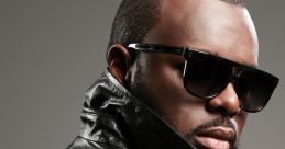 Maître Gims poses confidently in a stylish black leather jacket and sunglasses, showcasing his signature look.