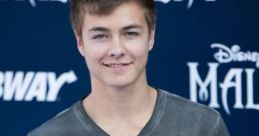 Peyton Reimer smiles at the premiere of Disney's Maleficent, showcasing a casual grey shirt and youthful charm.