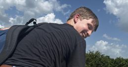 Smiling young man in casual attire poses playfully outdoors, showcasing a fun, carefree moment against a sunny backdrop.
