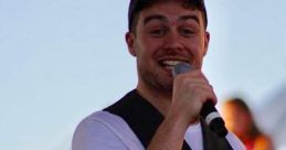 Mikey Fitzpatrick O'Dwyer performs energetically on stage with a microphone, engaging a lively audience in the background.