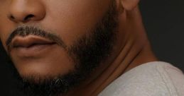 Close-up portrait of a man with a well-groomed beard, wearing a gray shirt, exuding confidence and charisma.