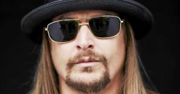Kid Rock poses confidently in a black leather jacket, sunglasses, and a stylish hat, showcasing his unique rock style.