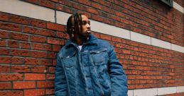 Young man in stylish denim jacket and distressed pants poses against a brick wall, showcasing modern urban fashion.