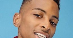 Funnymike showcasing his signature style with flashy jewelry, vibrant attire, and confident smile against a blue background.