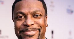 Chris Tucker smiling in a black tuxedo with a bow tie, exuding charm at a red carpet event. Iconic comedian and actor.