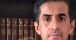 Portrait of a man with a neutral expression, standing in front of a bookshelf filled with classic literature.