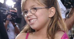 Cheerful child in a pink dress, smiling at a media event, capturing the joy of youth and celebration.