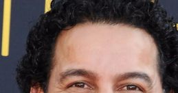 Miguel smiles brightly, showcasing his curly hair and warm expression at a public event, radiating charm and charisma.