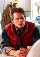 Marty McFly, portrayed by Michael J. Fox, looks thoughtful in a diner, wearing a signature red vest and checkered shirt.