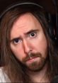 Asmongold showcasing a thoughtful expression, wearing headphones, with long hair and a beard, in a gaming setup.