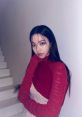 AESPA Karina poses elegantly in a red sweater, showcasing her striking features against a minimalist background.