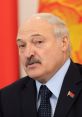 Lukashenko, President of Belarus, delivers remarks with national flag in the background, showcasing his serious demeanor.