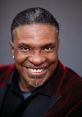 Keith David, known for his role in Spawn, smiles warmly in a stylish black and red outfit against a neutral background.