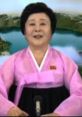 Enthusiastic North Korea newsreader Ri Chun-hee in traditional hanbok, broadcasting from a scenic backdrop.