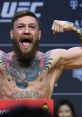 Conor McGregor flexes with excitement at a UFC weigh-in, showcasing his tattoos and powerful physique.