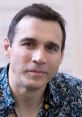 Adrian Paul with a thoughtful expression, wearing a patterned shirt, showcasing his charm and charisma at a convention.