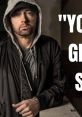 Eminem in casual wear, leaning against a wall with a serious expression, showcasing his iconic style and confidence.