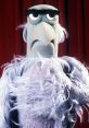 Sam the Eagle, a Muppet character by Frank Oz, displays a serious expression against a red curtain backdrop.