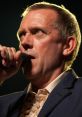 Hugh Laurie passionately singing into a microphone, showcasing his talent and charisma on stage.