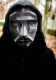 Front Man from Squid Game wearing a geometric mask and hood, set against a blurred outdoor background.