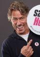 John Bishop smiling and holding a sign promoting kindness, wearing a "say hello" badge for awareness campaign.