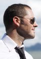 Profile of Serpentza, known for his insights into life in China, wearing sunglasses and a dress shirt against a scenic backdrop.