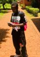 Young man standing outdoors, wearing a graphic t-shirt and sweatpants, focused on his phone amidst lush greenery.