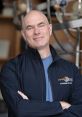Scott Manley, renowned science communicator, poses confidently with arms crossed in a lab setting surrounded by equipment.