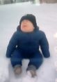 Baby playing in the snow, wearing a blue snowsuit and a black hat, expressing joy in a winter wonderland.