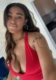 Woman in a deep red dress with a stylish tattoo, smiling confidently in a modern interior setting.