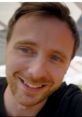 Smiling young man with light brown hair and blue eyes, sharing insights on tech and gadgets in a casual setting.