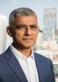 Sadiq Khan in a formal suit, confidently posing against a city skyline backdrop, showcasing leadership and ambition.