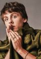 Jacob Bertland poses thoughtfully in an olive green jacket, showcasing unique jewelry and expressive features.