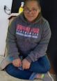 Jimena Friend sitting cross-legged in a cozy gray hoodie, smiling with glasses in a home setting.