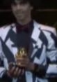 King Sammelot wearing a stylish black and white suit, holding a golden trophy at a prestigious award ceremony.